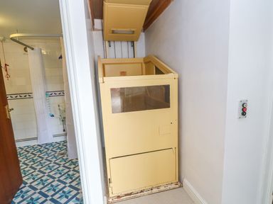 A narrow beige stair lift next to a bathroom with patterned floor tiles and a shower curtain at The Stables in Longrock