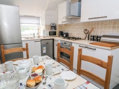 A kitchen with a dining table set with teapot mugs scones and condiments at The Stables in Longrock