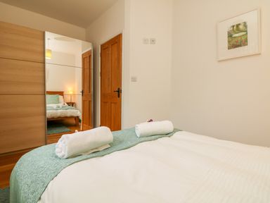 A bedroom with a bed covered with white bedding and green runner with rolled towels two wooden doors a large mirror and a framed picture on the wall at Sunset in St Just