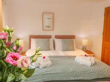 A bedroom with a double bed two bedside tables with lamps towels on the bed and flowers in the foreground at Sunset in St Just