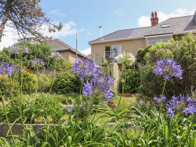 A garden with purple and white flowers and a house with a balcony in the background at Sunset in St Just