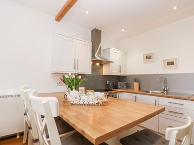 A kitchen with a wooden table and white chairs a tray with cups and flowers and white cabinets at Sunset in St Just