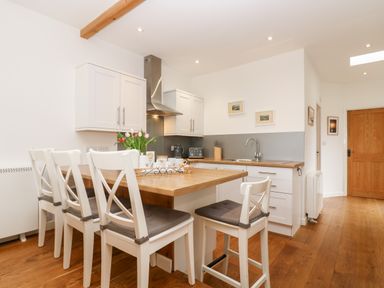 A kitchen with wooden floors a wooden table with four white chairs white cabinets and a stainless steel range hood at Sunset in St Just