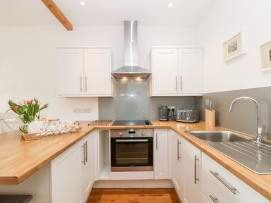 A kitchen with white cabinets wooden countertops a stainless steel oven and hood a sink toaster kettle and flowers on the counter at Sunset in St Just