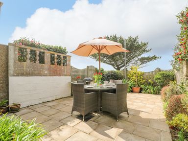 A patio with a table and four chairs under an umbrella surrounded by plants and a stone wall at Sunset in St Just
