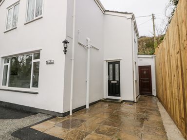 The exterior side of a white building with two doors a wooden fence and paved ground at Avalon in St Agnes