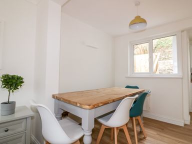 A dining area with wooden table four chairs and a small plant on a cabinet by a window at Avalon in St Agnes