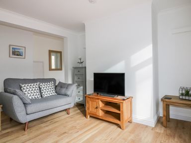 A living room with a grey sofa a wooden TV stand with a television a wooden side table and a chest of drawers at Avalon in St Agnes