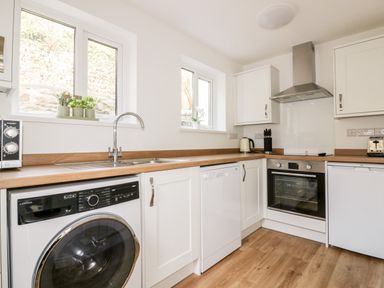 A kitchen with white cabinets wooden countertops washing machine dishwasher oven and range hood at Avalon in St Agnes