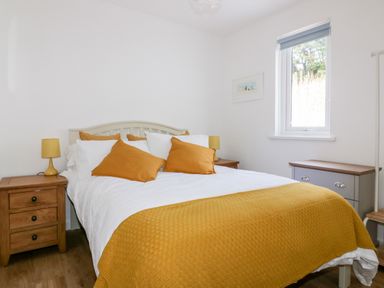 A bedroom with a double bed with yellow pillows and throw a wooden nightstand with a yellow lamp and a window at Avalon in St Agnes