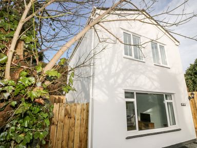 A white two-story house with large windows and a wooden fence next to a tree with green leaves at Avalon in St Agnes