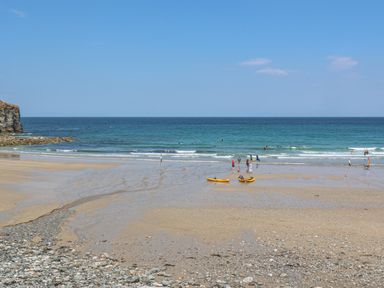 A beach with people near the water and kayaks on the sand at Avalon in St Agnes