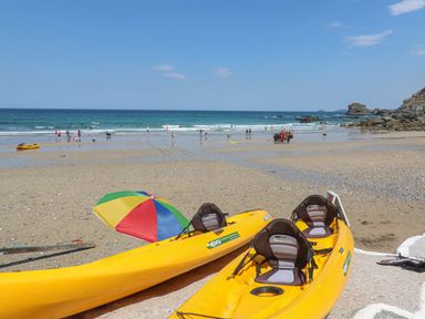 A sandy beach with yellow kayaks and a colorful umbrella near the water at Avalon in St Agnes