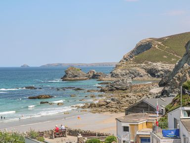 A rocky beach with people on the sand and near the water with buildings and cliffs in the background at Avalon in St Agnes