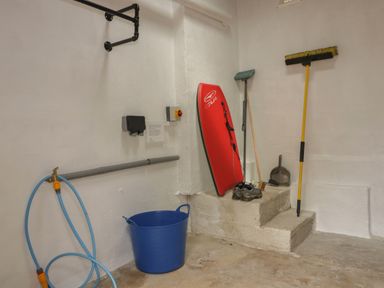 A storage room with a red bodyboard shoes a broom dustpan a blue bucket and a hose at Avalon in St Agnes