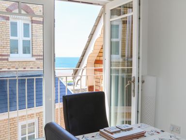An open glass door leading to a balcony with a view of the sea two black chairs and a table with a patterned cloth at Seashore in Woolacombe