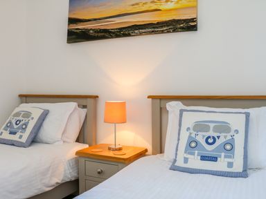 A bedroom with two single beds with coastal themed cushions and a bedside table with a lamp at Seashore in Woolacombe