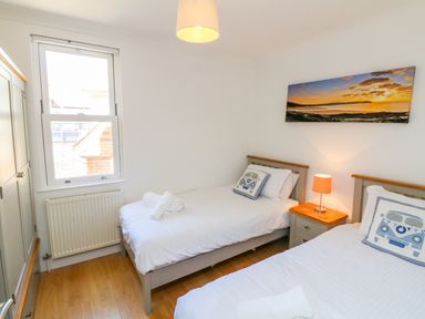 A bedroom with two single beds a nightstand with a lamp a window and a wardrobe at Seashore in Woolacombe