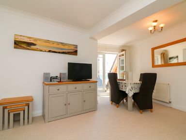 A dining area with a table and four chairs next to a sideboard with a television and stereo at Seashore in Woolacombe