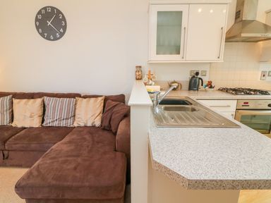 A brown sofa with cushions and a kitchen counter with a sink kettle and stove at Seashore in Woolacombe