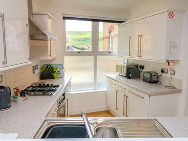 A kitchen with stove microwave toaster and sink with a window showing a view of hills at Seashore in Woolacombe