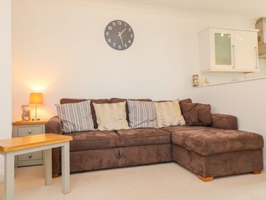 A brown sectional sofa with striped and solid pillows in a living room with a clock on the wall and a side table with a lamp and jar at Seashore in Woolacombe