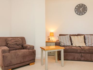 A living room with brown sofas a wooden table a side table with a lamp and a wall clock at Seashore in Woolacombe