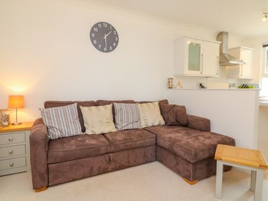 A living room with a brown sofa cushions a side table with a lamp and a small wooden table in front with a kitchen in the background at Seashore in Woolacombe