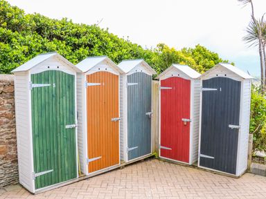 Five small wooden sheds with numbered colored doors on a paved area near greenery at Seashore in Woolacombe