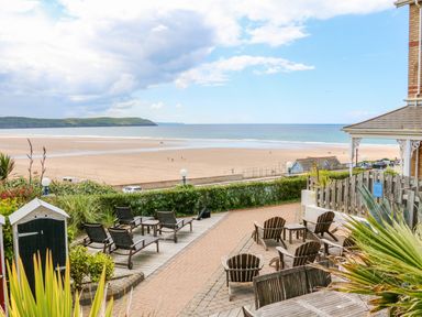 An outdoor patio with wooden chairs and lounge chairs overlooking a sandy beach and ocean at Seashore in Woolacombe