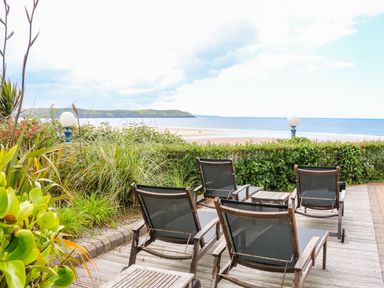 A patio with four lounge chairs and tables overlooking a beach and ocean at Seashore in Woolacombe