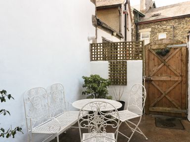 A small outdoor patio with white metal table and chairs and a wooden gate at St Mary's Cottage in Windermere