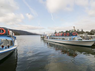 A lake with two docked passenger boats and hills in the background at St Mary's Cottage in Windermere
