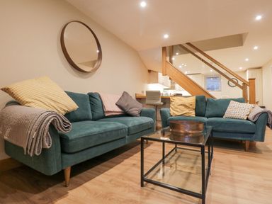 A living room with two green sofas and a glass coffee table under wooden stairs at St Marys Cottage in Windermere