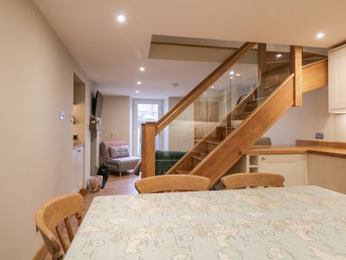 A dining table with map design and wooden chairs near a wooden staircase with glass panels at St Mary's Cottage in Windermere