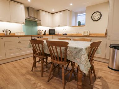 A kitchen with wooden chairs around a table covered with a map-patterned tablecloth and cabinetry along the walls at St Mary's Cottage in Windermere