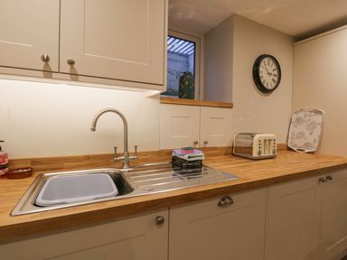 A kitchen countertop with a sink and faucet a toaster a stack of cloths and a wall clock at St Mary's Cottage Windermere