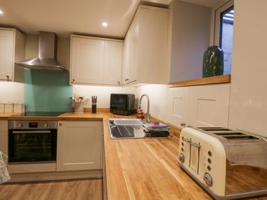 A kitchen with wooden countertops white cabinets a toaster oven a kettle a sink and a teal vase on a windowsill at St Mary's Cottage in Windermere