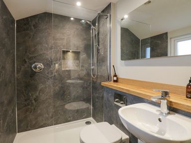 A bathroom with a shower, toilet, sink, mirror, and wooden countertop at St Mary's Cottage in Windermere