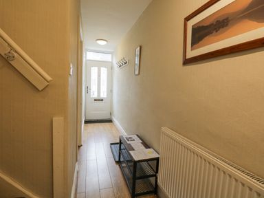 A narrow hallway with a white front door a small black shelving unit and a wall-mounted radiator at St Mary's Cottage in Windermere