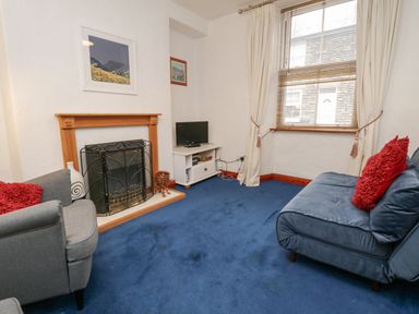 A living room with a fireplace a small TV on a stand and sofas with red cushions at St Marys Cottage in Windermere