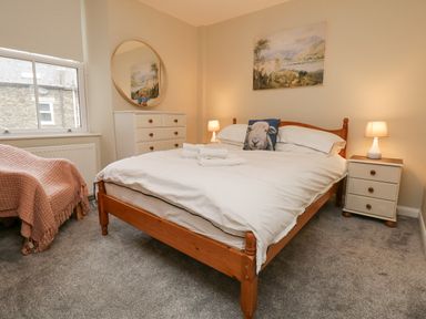 A bedroom with a wooden bed frame bedside tables lamps a chest of drawers and an armchair at St Mary's Cottage in Windermere