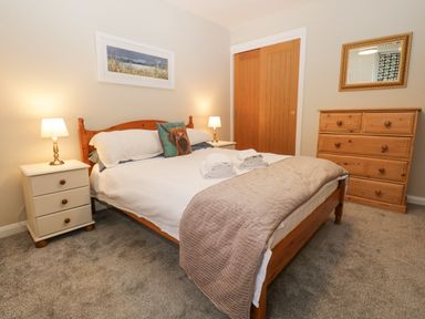 A bedroom with a double bed with white bedding and folded towels two bedside tables with lamps a wooden chest of drawers a mirror and a framed picture at St Marys Cottage in Windermere