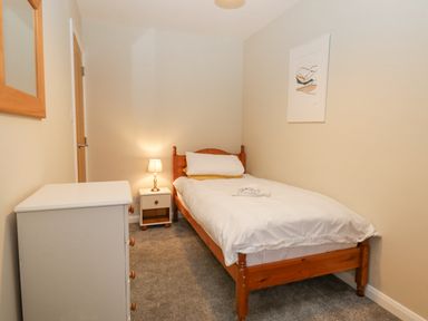 A small bedroom with a single wooden bed a white dresser a bedside table with a lamp and a framed picture on the wall at St Mary's Cottage in Windermere