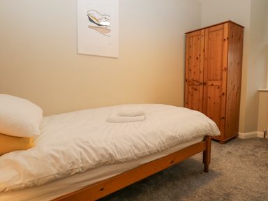 A bedroom with a single bed with white bedding and folded towels on top and a wooden wardrobe against the wall at St Mary's Cottage in Windermere