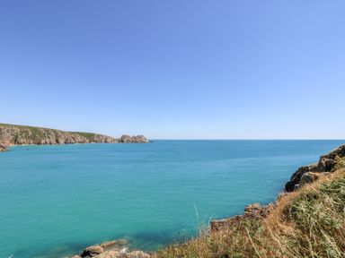 A coastal view with rocky cliffs and blue sea under a clear sky at The Upper Deck in Porthcurno