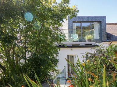 An outdoor view of a two-story house with a balcony and greenery at The Upper Deck in Porthcurno