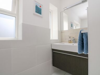 A bathroom sink with a mirror above and two windows next to it with a blue towel hanging on the side at The Upper Deck in Porthcurno