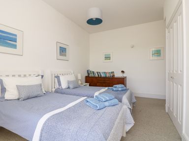 A bedroom with two single beds side by side with blue bedding a wooden dresser with books on top and framed pictures on the walls at The Upper Deck in Porthcurno