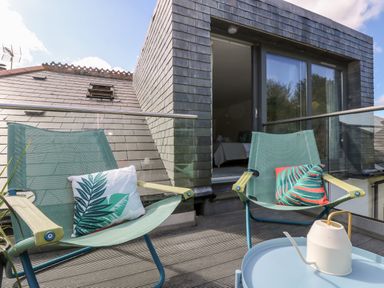 A balcony with two chairs and cushions and a watering can on a table at The Upper Deck in Porthcurno